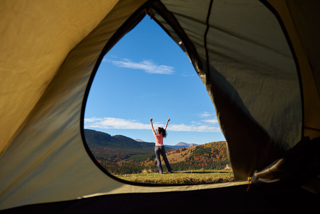 徒步旅行年轻女子在旅游帐篷前 从里面看 背景是木本小山和蓝天徒步旅行周末自然