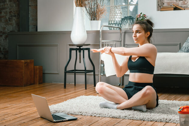 锻炼特写镜头中 一位身穿运动服的年轻女子正在休息 在家里的地板上伸展 在笔记本电脑上看电影和学习 这是一个社交网络健康笔记本电脑体操