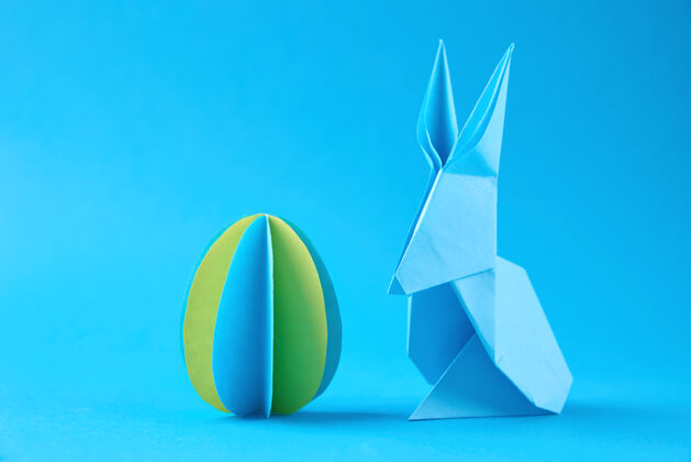 手工蓝色墙上的纸折纸兔和彩蛋复活节庆祝概念兔子文化复活节