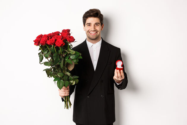 礼物穿着黑色西装 手持玫瑰和订婚戒指 面带微笑的帅哥浪漫关系玫瑰