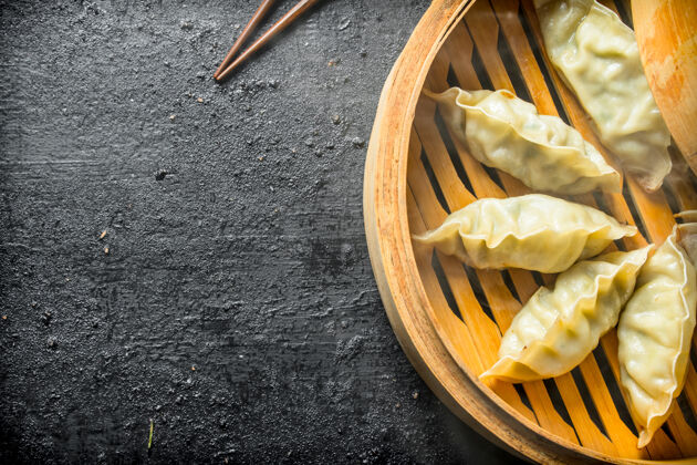 顶视图香喷喷的中国葛根饺子放在一个竹蒸笼里 放在一张黑色的乡村桌子上热服务饺子