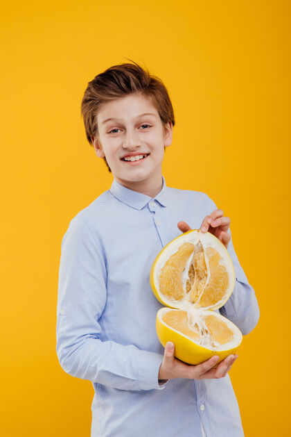 肖像快乐的小男孩手里拿着柚子 奇异的水果 香蕉和橘子 穿着蓝色的衬衫 隔离在黄色的墙上休闲微笑柚子水果