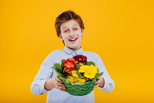 玫瑰快乐的小男孩手里拿着花篮 穿着蓝色衬衫 孤零零地站在黄色的墙上孩子微笑男孩