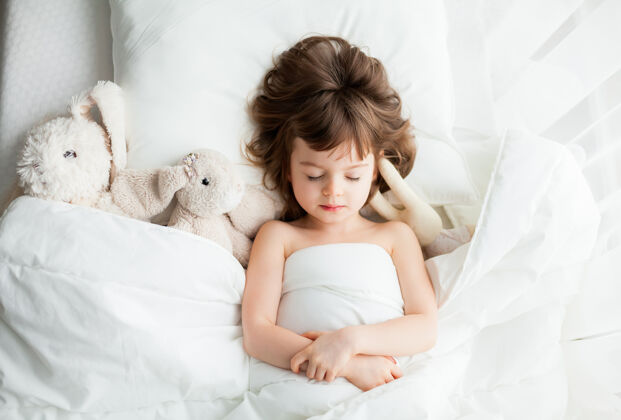 休息可爱安静的小女孩睡在白色的床上 旁边有兔子玩具可爱舒适枕头