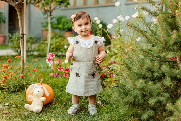 生活方式快乐的女婴站在五颜六色的花园里 带着南瓜 鲜花和玩具微笑白天草