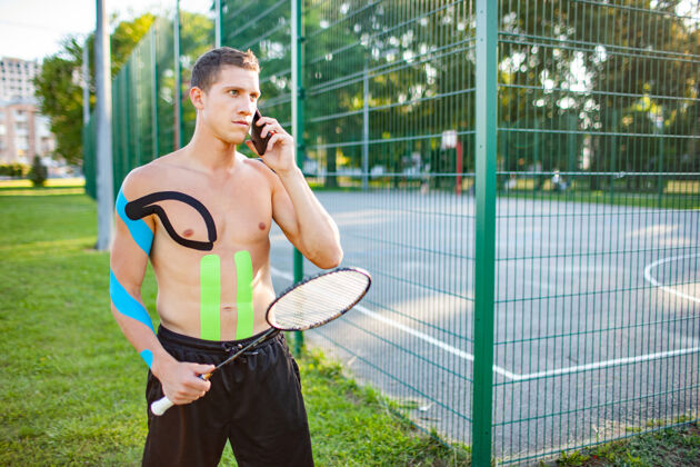 康复年轻的白种人职业网球运动员 在有围栏的运动场附近拿着球拍 身上贴着运动录像带活动物理受伤