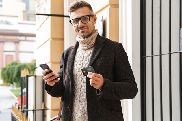 支付帅哥穿着外套走在户外 用手机和信用卡在网上购物支付购物城市