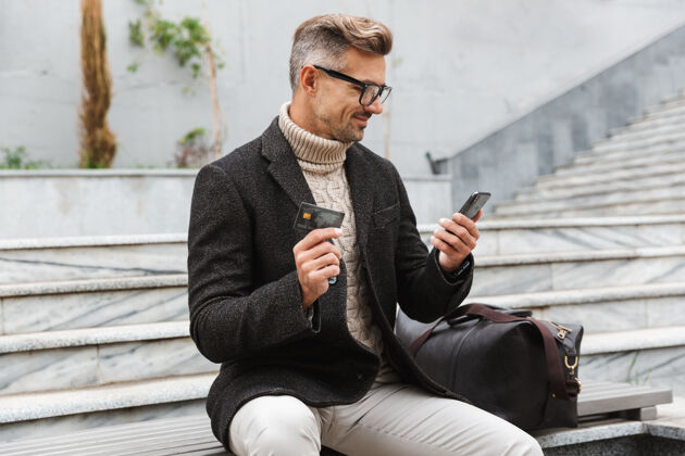 电话帅哥穿着夹克坐在户外用手机和信用卡上网购物城市网络设备
