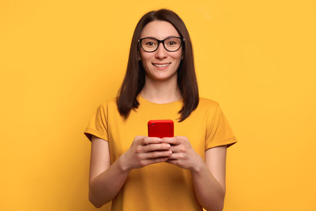 休闲戴着眼镜的棕色头发微笑的年轻女子在智能手机上输入短信牙齿微笑愉快