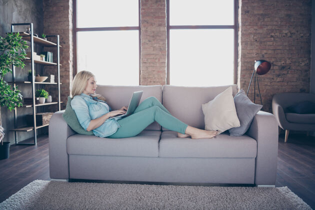 自由职业者侧面图女士躺在沙发床上使用笔记本电脑的肖像时尚上网本时尚