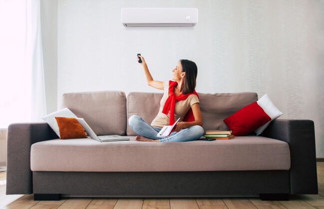 家用电器美丽的现代黑发女人坐在沙发上休息 在炎热的日子里使用空调温度空调空调