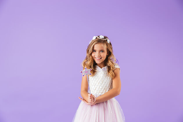 魔术一个微笑的可爱女孩的肖像 穿着公主裙 隔着紫罗兰色的墙 手里拿着魔杖微笑童年表情