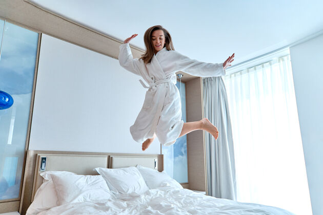 房子在一个酒店房间里 一个穿着浴衣的快乐有趣的女人在快乐的时刻跳上了床感觉良好 享受生活的理念轻松的生活方式放松舞蹈室内