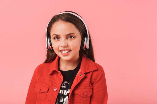微笑画面中快乐的小女孩戴着休闲耳机听音乐 隔着红墙孤立着黑发站音乐