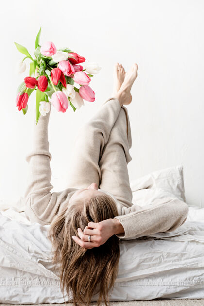 人幸福的女人穿着睡衣躺在床上 双手捧着鲜艳的郁金香花束女性浪漫年轻