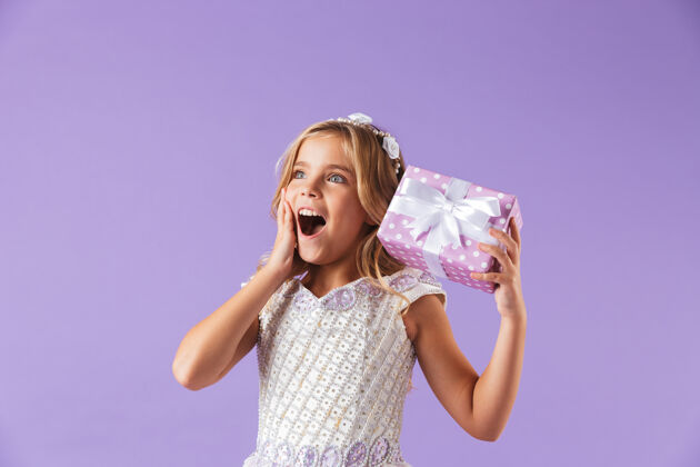 肖像一个微笑愉快的美丽女孩的画像 穿着公主裙 隔着紫罗兰色的墙 手里拿着礼物盒微笑惊喜魔术
