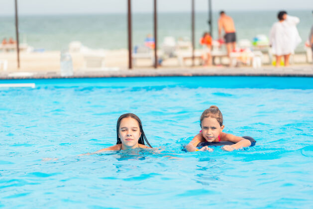 游泳池两个小姐妹在酒店附近的一个大游泳池里游泳 池里有我清澈的蓝色海水夏季阳光欢呼