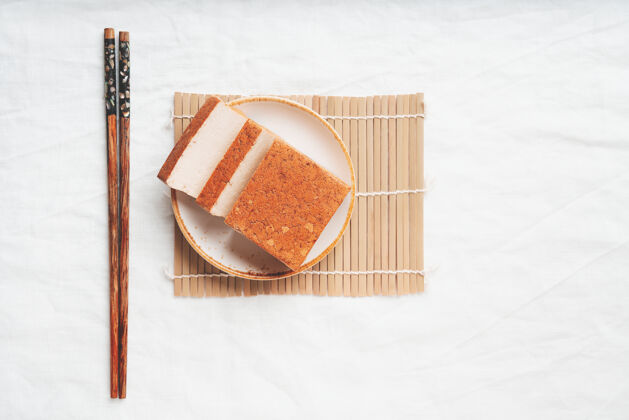 美味一块有机熟透的豆腐奶酪 放在白色盘子里 放在竹席上平铺顶视图素食小吃概念食物豆腐菜配料