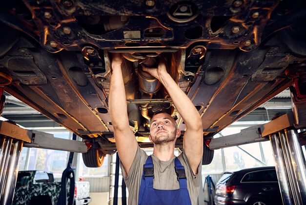 机械帅气的汽车修理工在加油站检查汽车的传动装置诊断修理工作