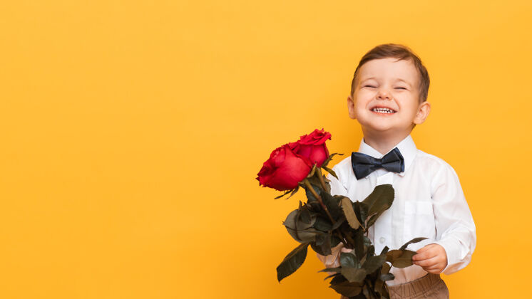 男性一个穿着白衬衫 白裤子 打着领结的男孩手里捧着一束红玫瑰 是给我妈妈的礼物可爱童年微笑