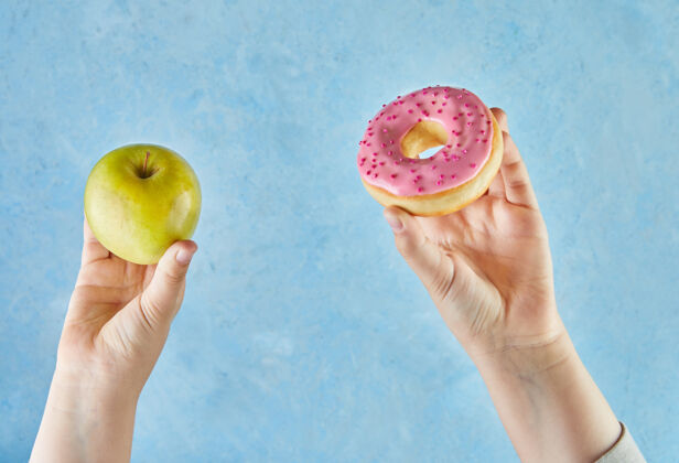 卡路里孩子们的手拿着苹果和甜甜圈 背景是蓝色的进退两难饮食健身