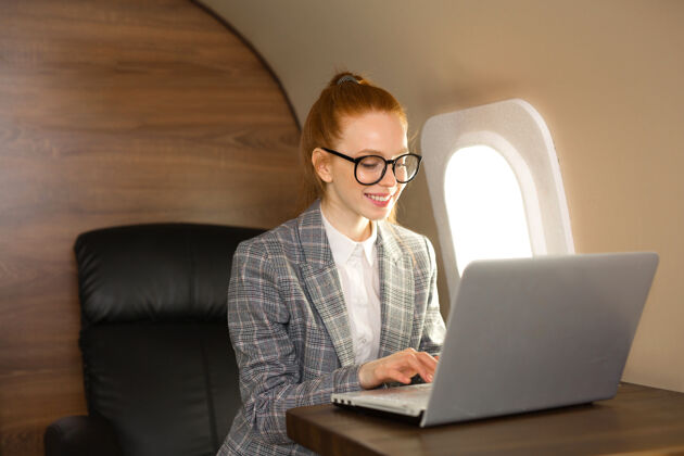 在线一位红发美女在机舱里拿着笔记本电脑商务微笑经理
