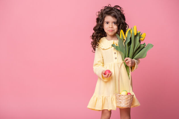 传统漂亮的小女孩拿着篮子 篮子里放着复活节彩蛋和郁金香 背景是粉红色的肖像春天微笑