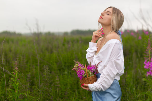草地性感美丽的女孩 穿着白衬衫 戴着粉色亮指甲 手里拿着一个紫色的花篮 站在田野里女人田野女性