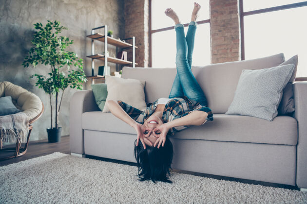乐趣全尺寸照片有趣的女士高兴地抬起腿倒过来显示奥基符号近眼睛眼镜形状躺在沙发上穿休闲服公寓室内舒适积极女性