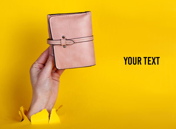 粉红色钱包女性手拿粉色钱包穿过撕破的黄色纸简约创意时尚概念.copy空间女性配件手