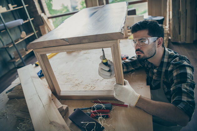 严肃顶部高角度聚焦工人更新平板家具木桌使用螺丝刀在家中车库工作钻头木材手套