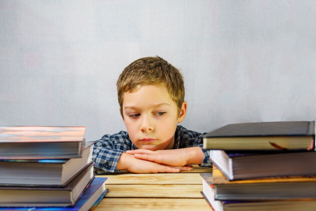 教育一个疲惫沮丧的小学生坐在木桌上的一堆书中间学习男孩小学生