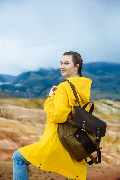 女孩一个年轻的微笑着的女孩背着一个背包在一座彩色的山的背景上旅游旅行者年轻人户外