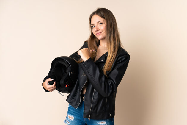 成人立陶宛年轻女子手持摩托车头盔孤立在米色背景自豪和自我满足成功年轻人胜利