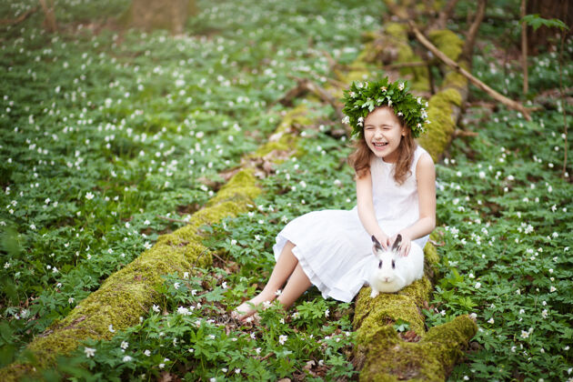 美丽穿着白色连衣裙的漂亮小女孩 在春天的树林里和白兔在一起海葵公园童年