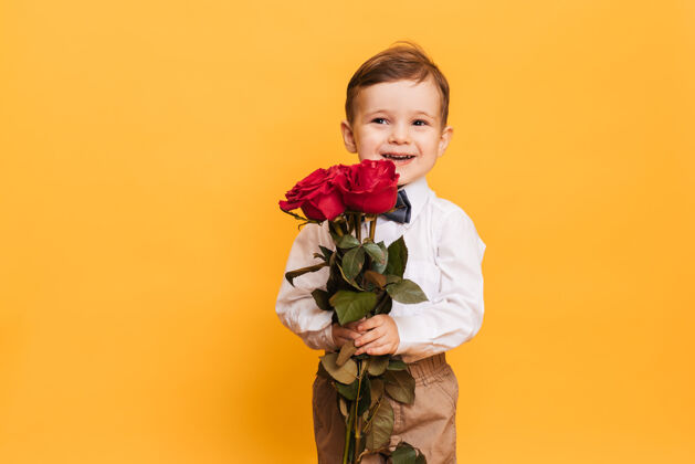欢呼一个穿着白衬衫 白裤子 打着领结的男孩手里捧着一束红玫瑰 是给我妈妈的礼物小玫瑰可爱