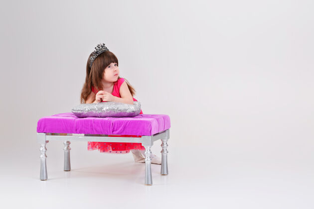 幼儿园穿着粉色公主裙 头戴皇冠 坐在灰色的粉色椅子上的漂亮的小黑发女孩背景可爱宝贝坐着公主年轻