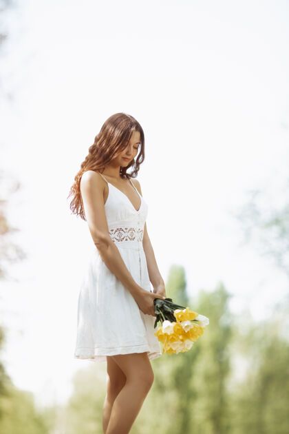 亚洲人一位身着白色连衣裙 手持一束春花的迷人女子 站在大自然的衬托下概念花快乐