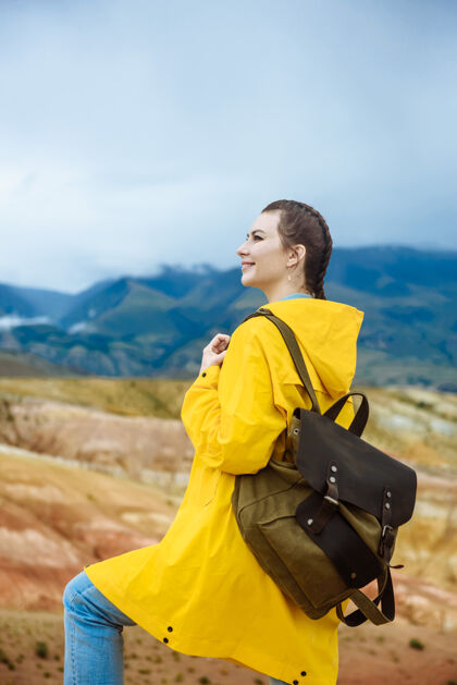 女人一个年轻的微笑着的女孩背着一个背包在一座彩色的山的背景上旅游背包自然岩石