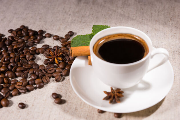 服务新鲜的黑咖啡在马克杯里放在白色盘子里 八角茴香和松豆子放在自然色调的画布上桌布咖啡屋休息