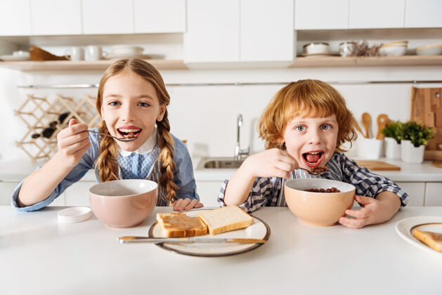健康最喜欢的味道不错令人钦佩的快乐的孩子们坐在餐桌旁 一边在厨房里吃麦片粥 为新的充满活力的一天做准备光明国内餐