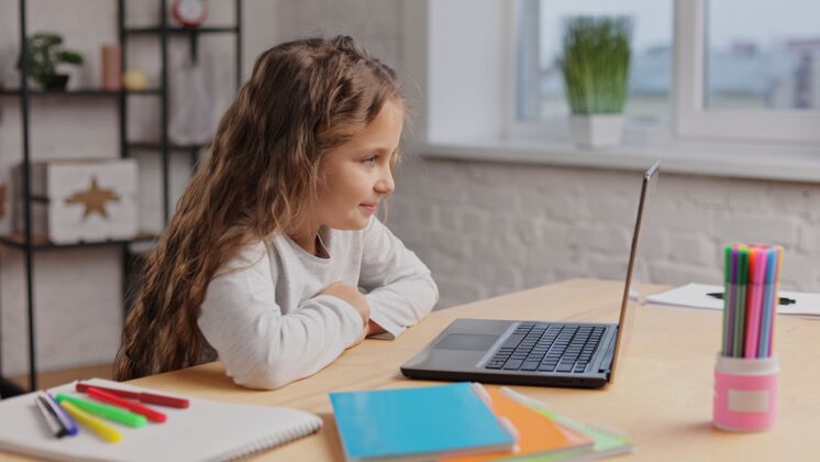 卡通快乐可爱的小女孩在电视上欣赏她最喜欢的卡通画的肖像笔记本电脑微笑小学生在电脑上看视频房子在线小
