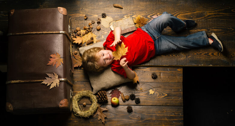 秋天心情儿童广告你的产品和服务.秋季概念金发秋天 小男孩趴在木地板上 趴着树叶休息离开孩子在秋天玩十二月季节阳光