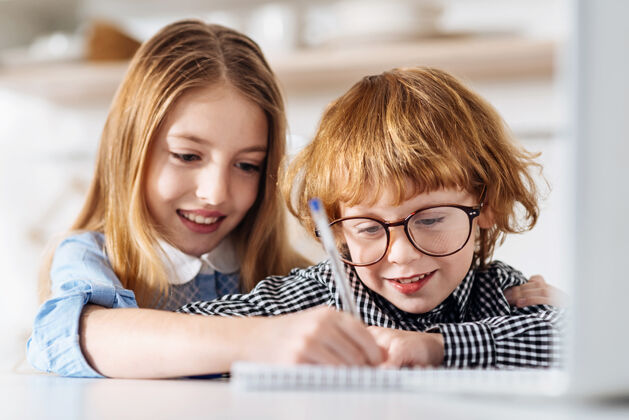 课平滑和整洁好奇可爱的红头发的孩子在他的姐妹们的帮助下写字 而他们都坐在桌边大脑姐妹千禧一代