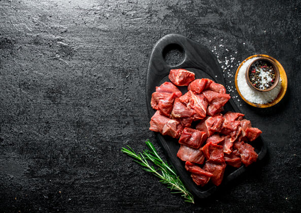 牛腰肉用迷迭香在黑色的砧板上切生牛肉食物营养块