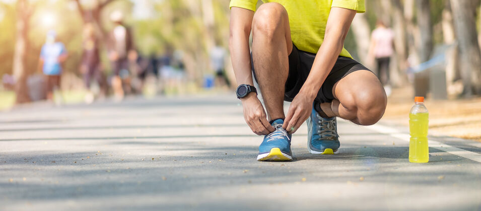 穿着年轻的运动员男子在公园户外系跑步鞋 男跑步者准备在外面的路上慢跑 亚洲健身步行和在公园的人行道上锻炼早上好健康和运动理念伸展卡路里道路