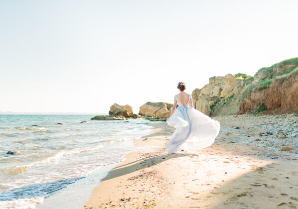 时尚背面是美丽的深色新娘穿着轻薄的雪纺婚纱绣着珠子在海边奔跑花束旅行新娘