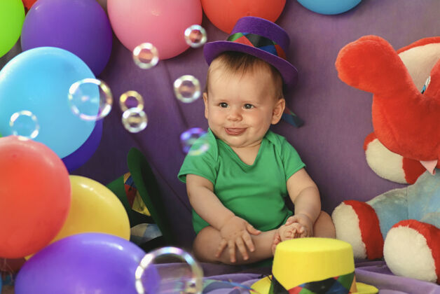 孩子男婴坐在一个有趣的节日气氛与气球和看肥皂泡肥皂泡宝贝坐