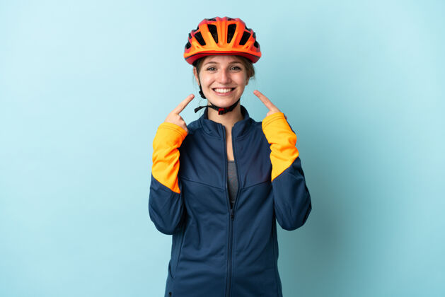 手势一个年轻的骑自行车的女人被隔离在蓝色的背景下竖起大拇指积极女人骄傲