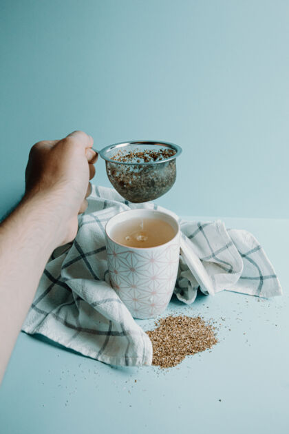 放松一只手抓住一个茶壶在一杯茶在一个柔和的蓝色背景倒时间茶碟
